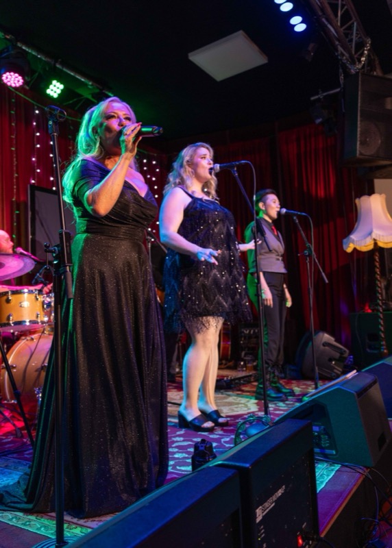 The three vocalists singing together on stage